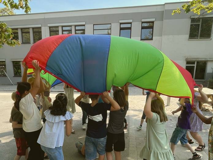 Schüler und Schülerinnen der künftigen Sekundarstufe spannen ein Buntes Tuch über ihren Köpfen