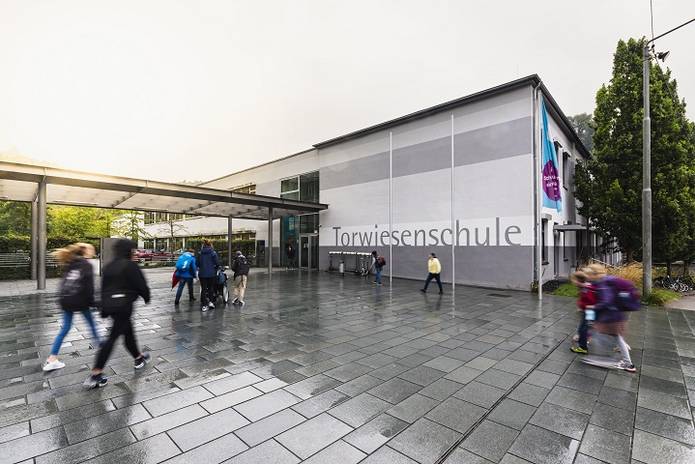 Der Haupteingang und das vordere Gebäude der Torwiesenschule an einem verregneten Morgen. Schüler bewegen sich Richtung Eingang.