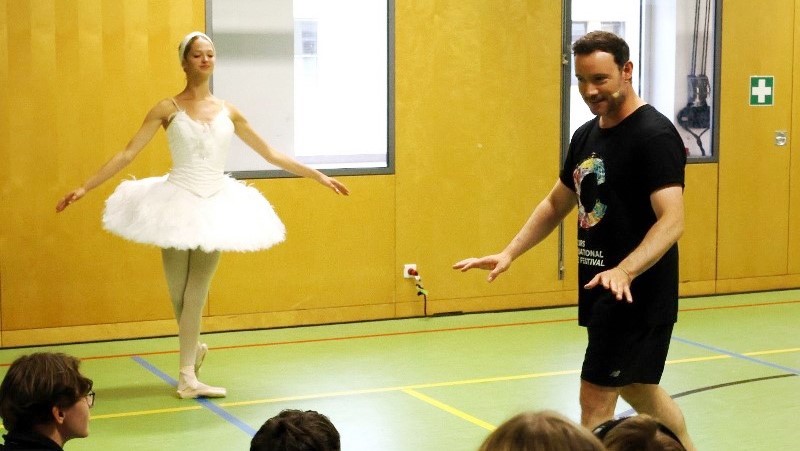 Eine Person spricht zu den Schülerinnen und Schülern über eine neben ihr stehende Ballerina der Gauthier Dance Juniors.